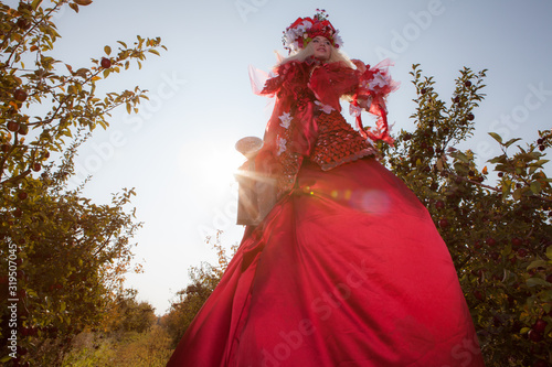 Sensual blond girl in fantasy red fairy tale stylization in apple park.