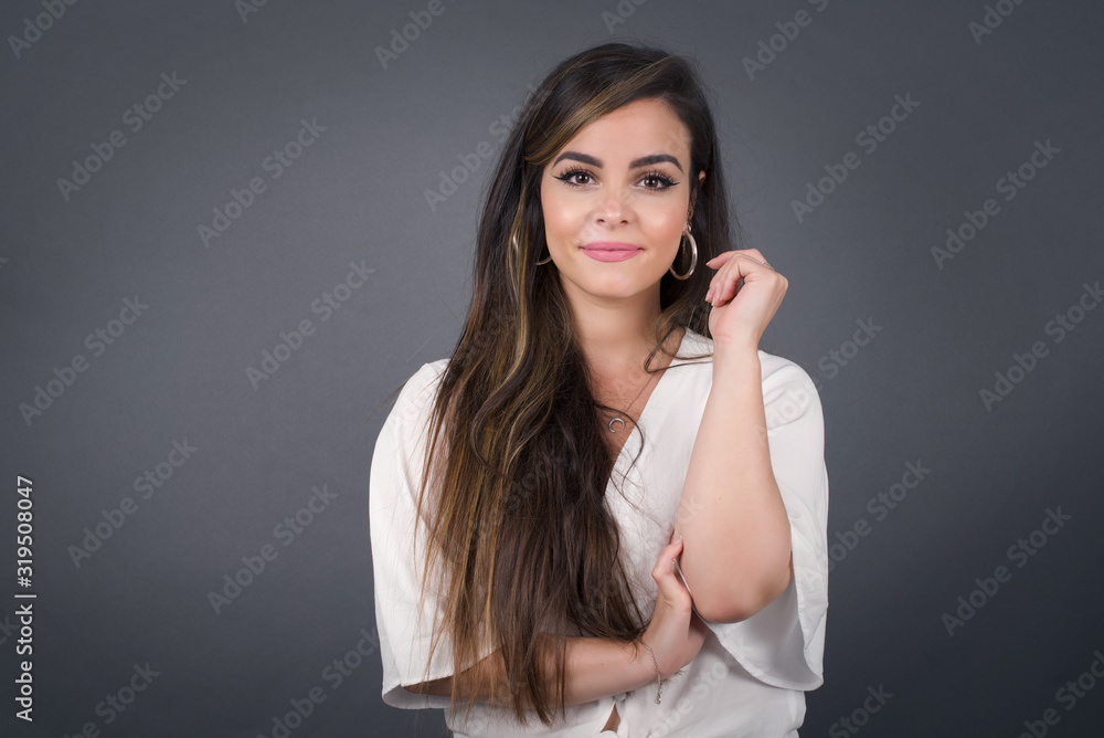 Image of cheerful pretty young caucasian lady standing against gray wall with hand near face. Looking with glad expression at the camera after listening to good news. Confident girl. Image of cheerful pretty young caucasian lady standing against gray wall with hand near face. Looking with glad expression at the camera after listening to good news. Confident girl.