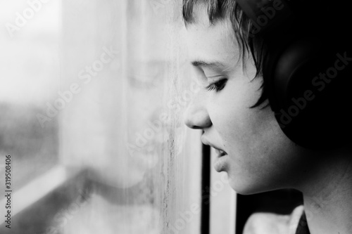 Teenage 12 years old boy looking through the window on the rain