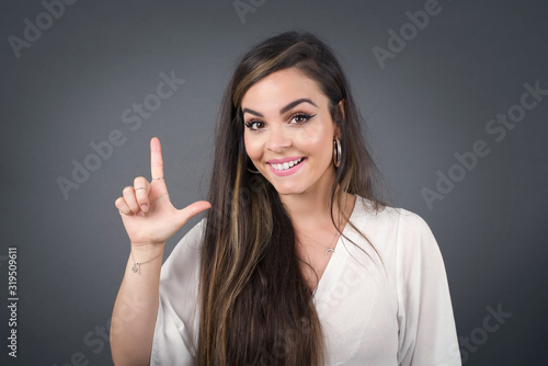 Close up portrait of pleasant looking blue eyed young woman model has clever expression, raises one finger, remembers herself not to forget tell important thing. Indoors