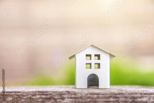 Miniature white toy model house in wooden background near green backdrop. Eco Village, abstract environmental background. Real estate mortgage property insurance dream home ecology concept