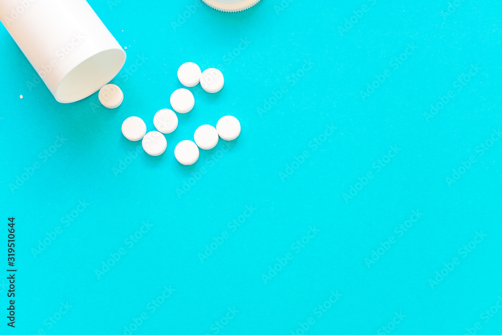 White pills dropped out of their container, on the top left corner, on a blue background, with copy space White pills dropped out of their container, on the top left corner, on a blue background, with copy space