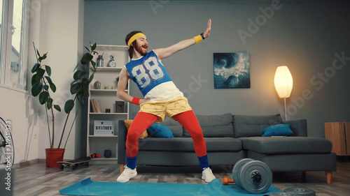 Funny stupid-looking reto fitness man dancing enjoying music and warming up on workout in the living room.
