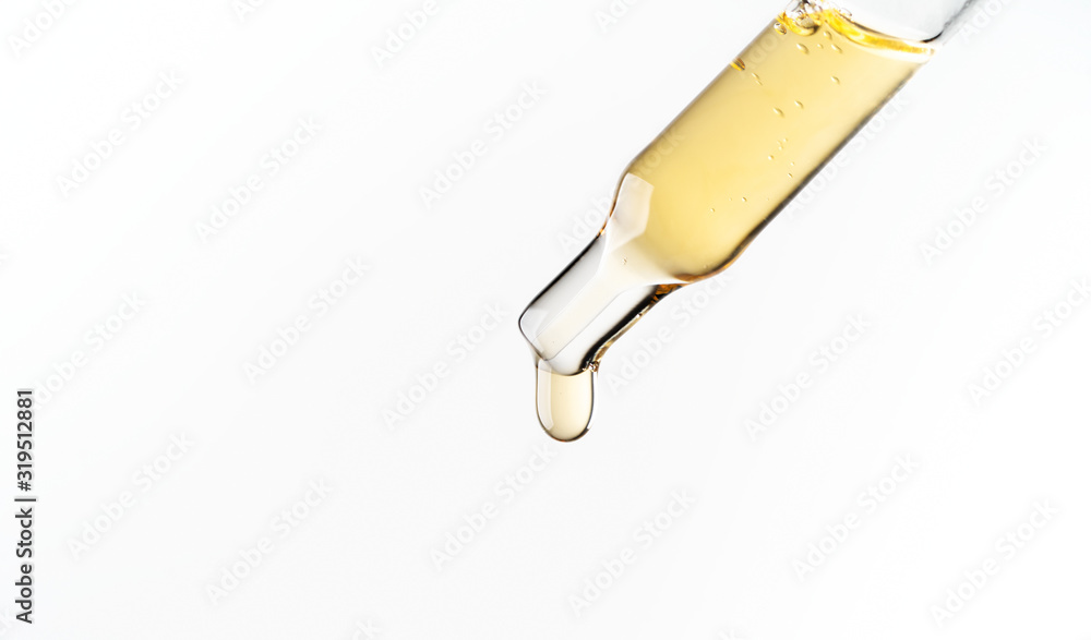 Cosmetic pipette with a liquid drop dripping close up on white background. Macro view transparent glass pipette. Concept of beauty, aromatherapy oil, medicine, vaccine development. Cosmetic pipette with a liquid drop dripping close up on white background. Macro view transparent glass pipette. Concept of beauty, aromatherapy oil, medicine, vaccine development.