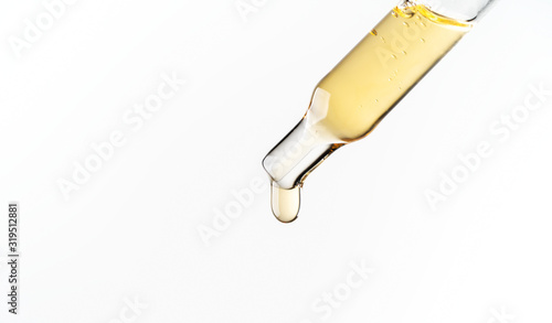 Cosmetic pipette with a liquid drop dripping close up on white background. Macro view transparent glass pipette. Concept of beauty, aromatherapy oil, medicine, vaccine development.