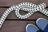 Blue and white striped sailor style shoes and rope with a knot on a brown wooden dock. Sailing and cruising concept. Top view travel background image. Space for text.