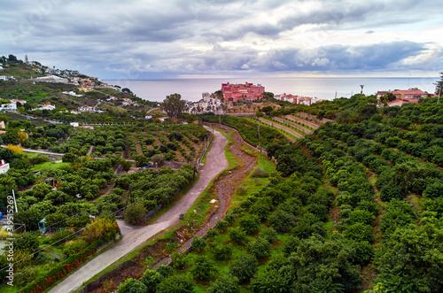 Almuñécar seaside hillside town aerial photo, above drone point of view. Picturesque hills, valleys, agricultural land scape. Moody cloudy sky over Mediterranean Sea. Granada province, Costa Tropical photo