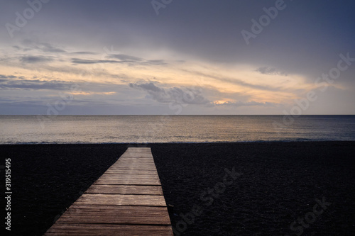 Fototapeta Naklejka Na Ścianę i Meble -  Beach of Calahonda in Costa del Sol, wooden boardwalk leading to Mediterranean Sea, fluffy cloudy sky romantic morning or evening sunrise. Spain, Andalusia.