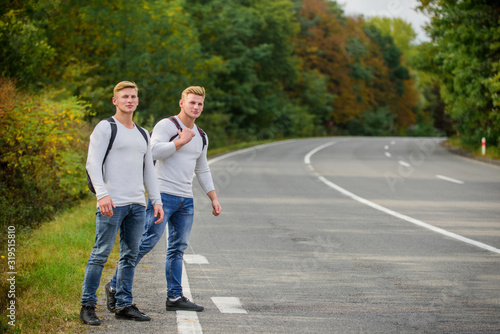 Twins men at edge of road nature background. Try to stop some car. Reason people pick up hitchhikers. Missed their bus. Need help. Cheap transport. Transport problem. Travel and transport concept