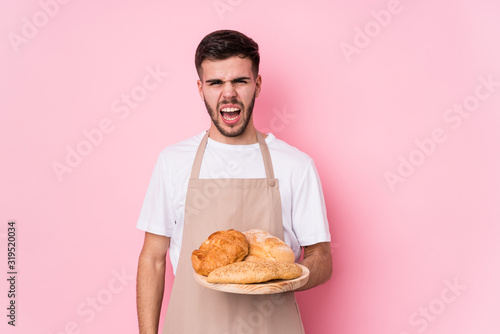 Young caucasian baker man isolated screaming very angry and aggressive.
