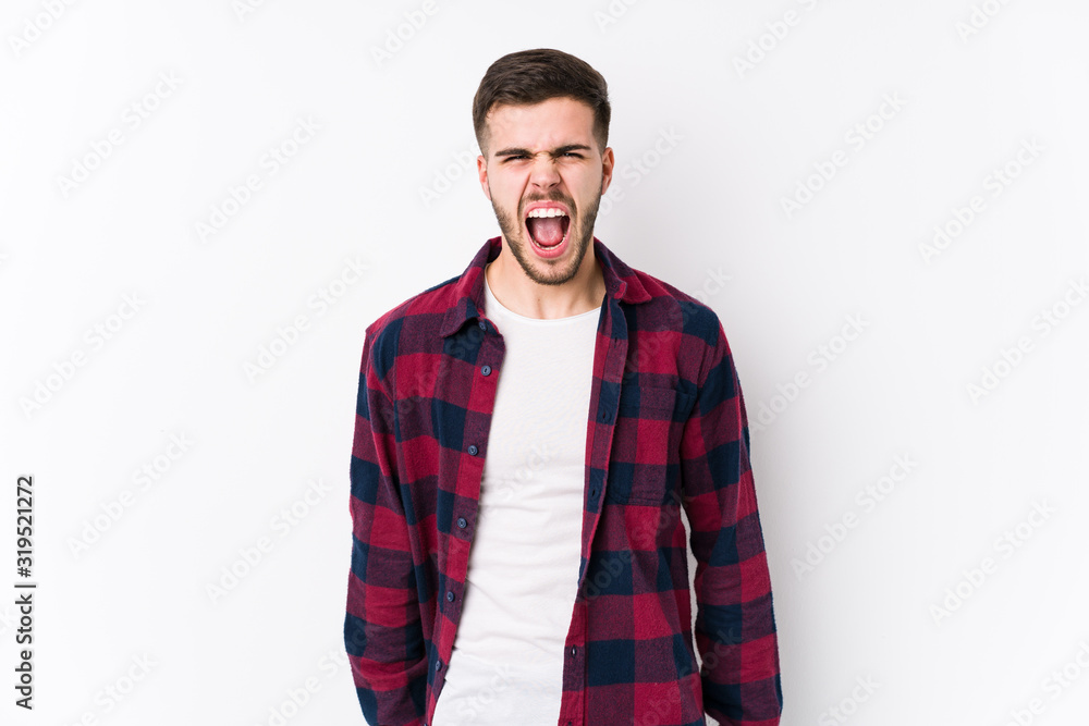 Young caucasian man posing in a white background isolated screaming very angry and aggressive. Young caucasian man posing in a white background isolated screaming very angry and aggressive.