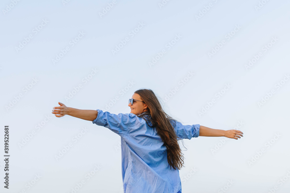 Young woman standing with hands up against blue sky achieving the top. longhair girl in a blue shirt with her arms raised up in the air feeling free and happy. female enjoying view, life, freedom Young woman standing with hands up against blue sky achieving the top. longhair girl in a blue shirt with her arms raised up in the air feeling free and happy. female enjoying view, life, freedom