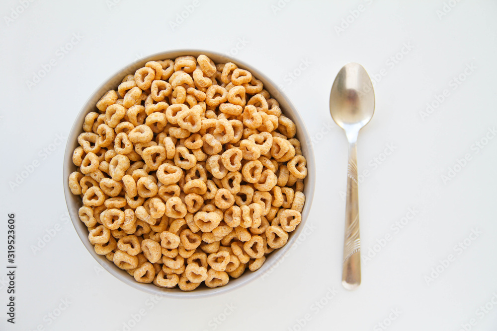 Bowl of whole grain oat cereal with a silver spoon on a white background , back view. Heart shapes cereal. 