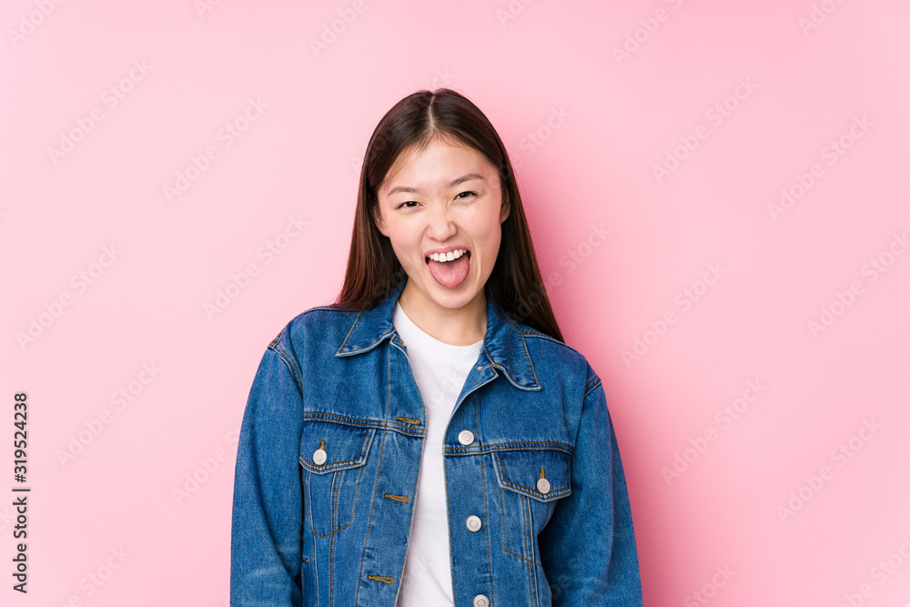 Young chinese woman posing in a pink background isolated funny and friendly sticking out tongue. Young chinese woman posing in a pink background isolated funny and friendly sticking out tongue.