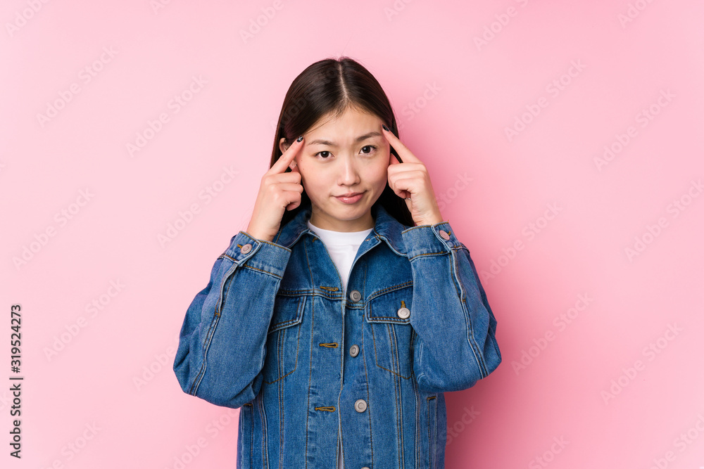 Young chinese woman posing in a pink background isolated focused on a task, keeping forefingers pointing head. Young chinese woman posing in a pink background isolated focused on a task, keeping forefingers pointing head.