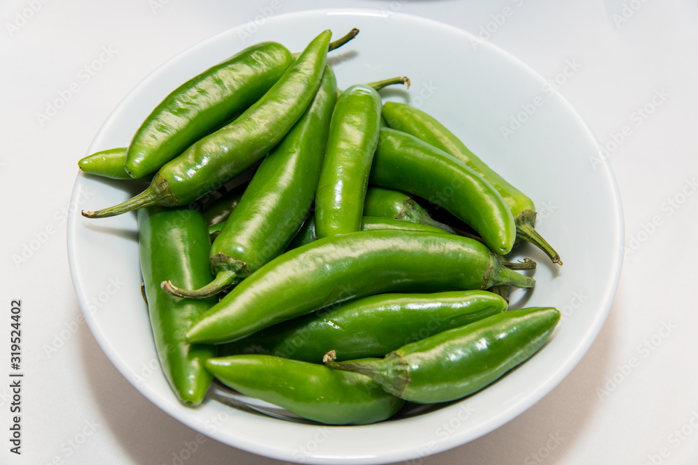 green hot peppers in a white plate over a white background green hot peppers in a white plate over a white background