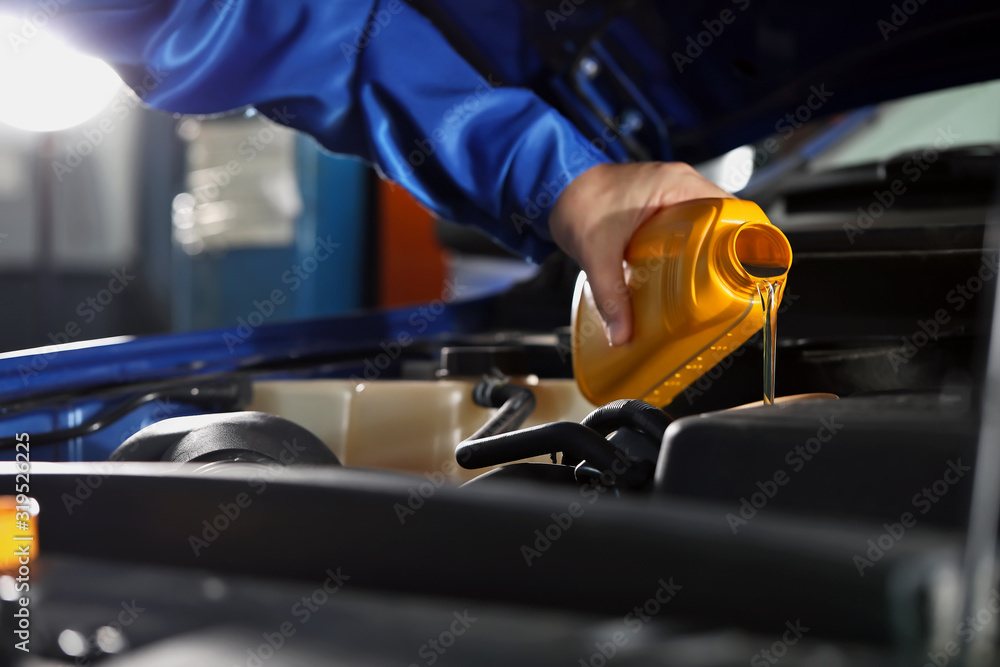 Male mechanic refilling car oil in service center