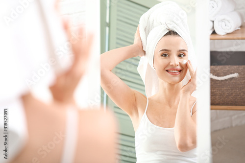 Beautiful young woman applying facial cream in front of mirror