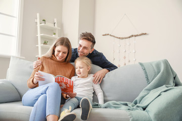 Happy young family reading fashion magazine while sitting on sofa at home