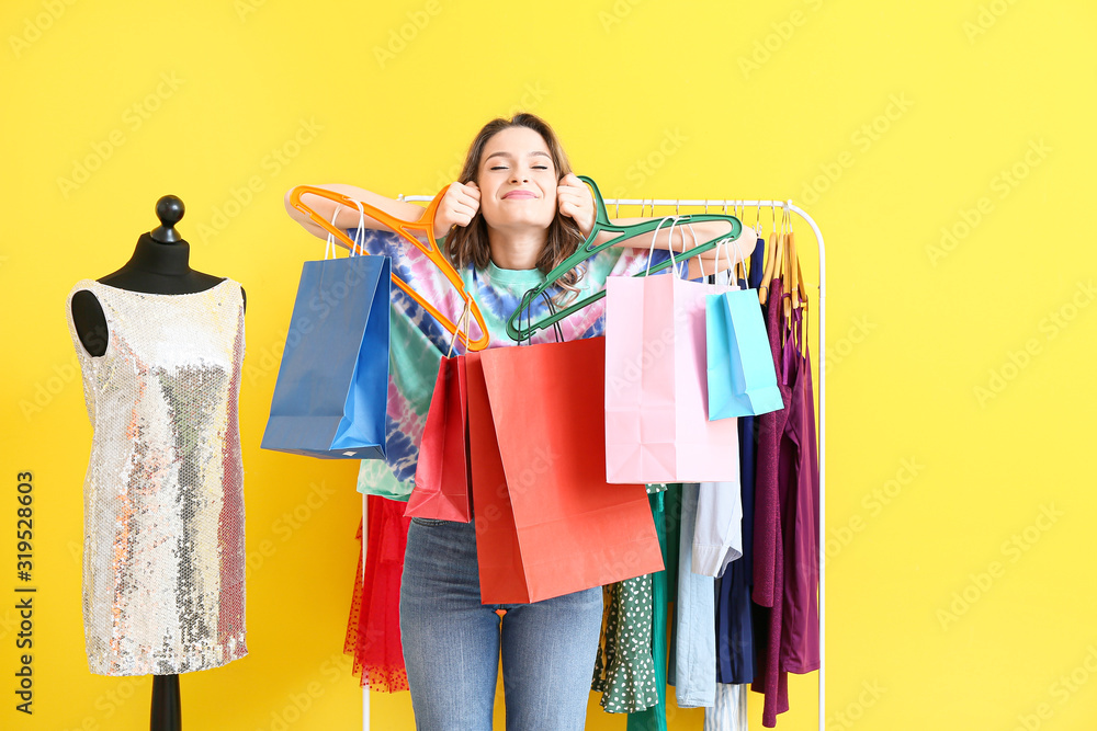 Female stylist with shopping bags near rack with modern clothes