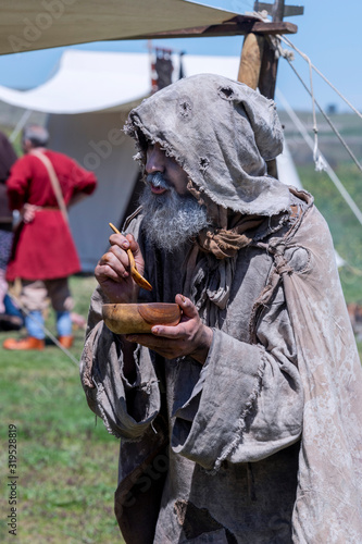 Middle-aged, bearded and ragged beggar, wandering a camp, looking for food photo