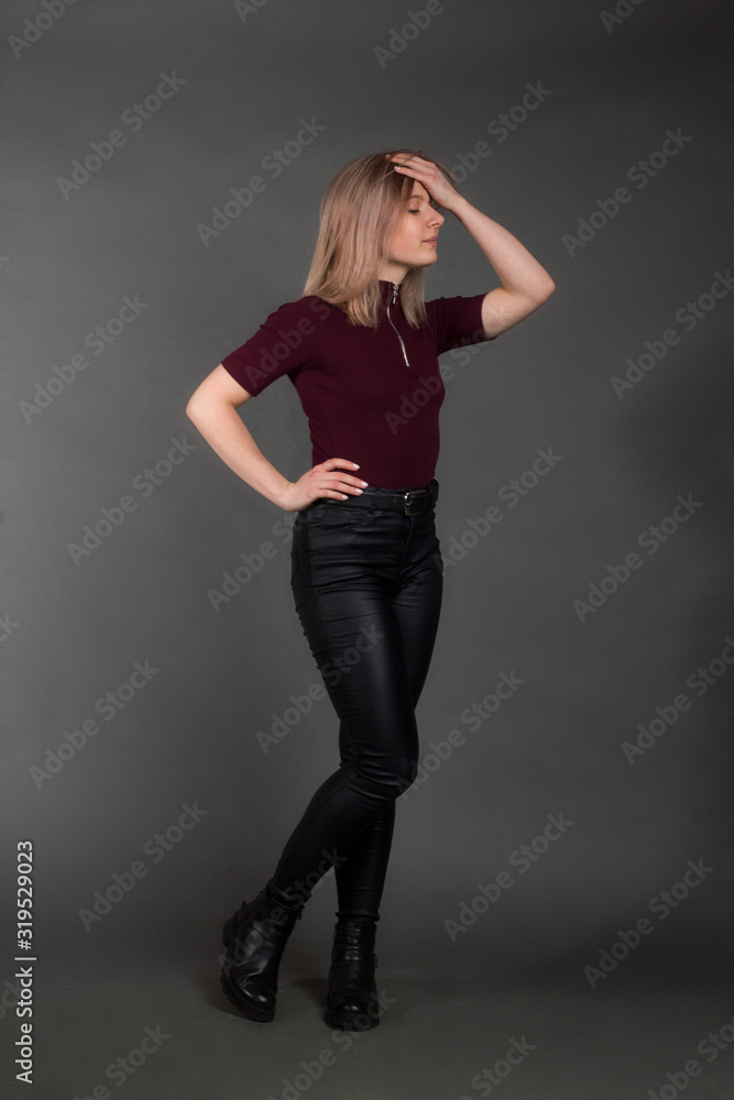growth Portrait of the blonde in the red sweater with short sleeves, leather trousers and boots. Studio shot on dark gray background