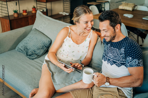 Happy relaxed couple sitting on couch in living room sharing a tablet photo