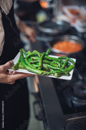 Chef holding plate with green asparagus in restaurant kitchen