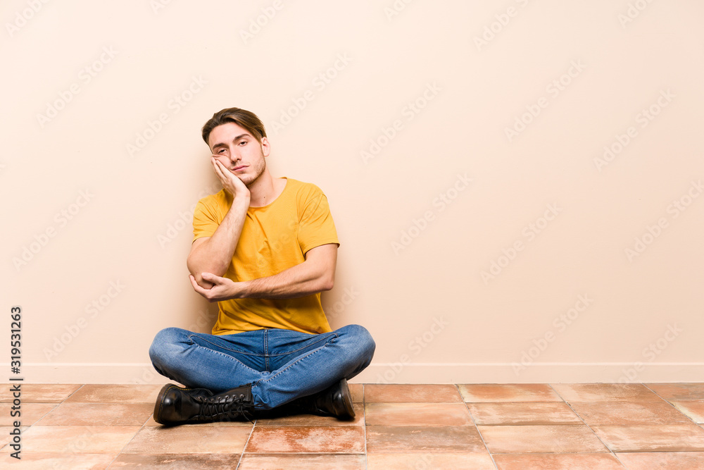 Young caucasian man sitting on the floor isolated who is bored, fatigued and need a relax day.
