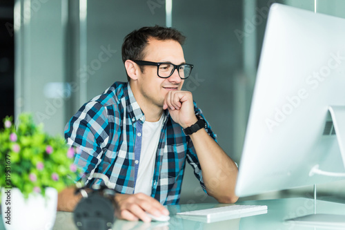 Young businessman in a checked shirt sitting working on a laptop at a table in the office