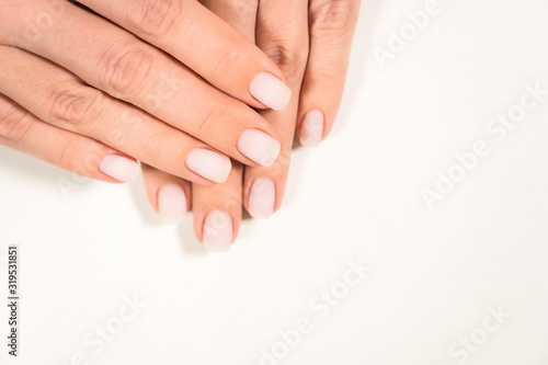 Closeup top view of two beautiful hands of woman with professional manicure  nails painted with light pink color and covered with mat top without gloss. Nude style design of fingernails.