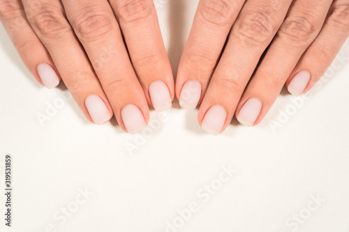 Closeup top view of two beautiful hands of woman with professional manicure  nails painted with light pink color and covered with mat top without glossy shine. Nude style design of fingernails.