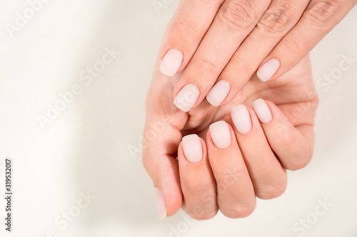 Closeup top view of 2 beautiful hands of woman with professional manicure  nails painted with light pink color and covered with mat top without glossy shine. Nude style design of fingernails.