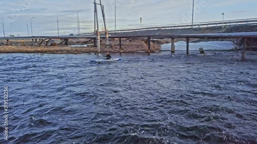 professional canoeist sails under grey bridge and gaspipe along raging river against cityscape under cloudy sky photo