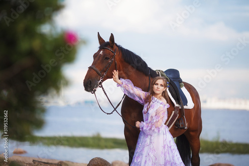 beautiful blond woman in a long green dress stands in a field among the herd of brown horse stallions. beautiful artistic emotional photo, wind develops her dress, cloudy sky