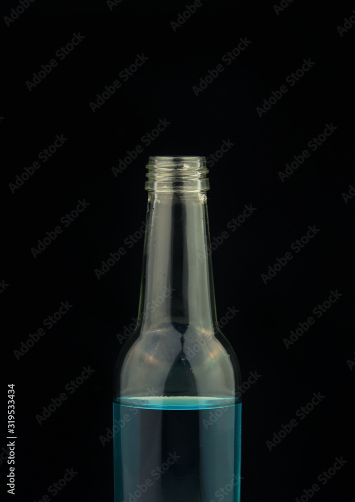 Glass bottle with blue water inside on black background.