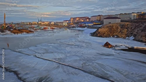 distant canoeist silhouette sails along river with white frozen parts passing town on brown banks aerial view