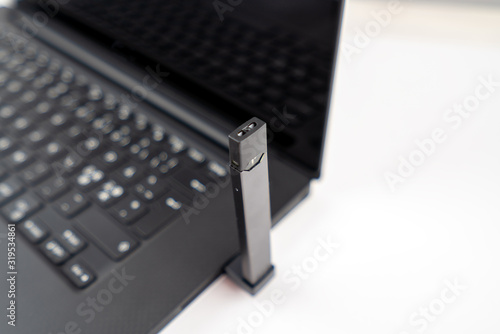 Vaping device charging with usb connection to laptop. Technology, nicotine e-cigarette concept. Copy space for text. photo