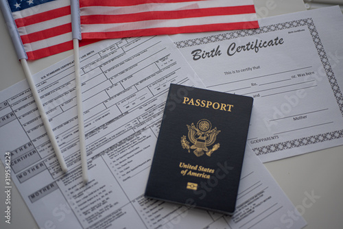 U.S. standard certificate of live birth application form next to flags of USA, passport of USA and Birth certificate blank. Birthright citizenship concept. Top view.