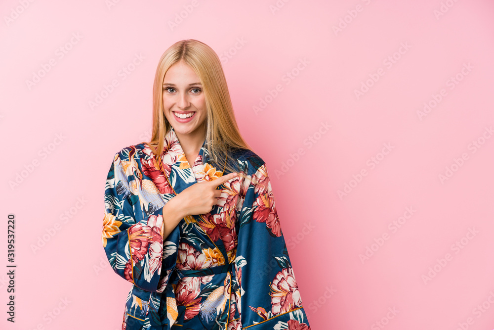 Young blonde woman wearing a kimono pajama smiling and pointing aside, showing something at blank space. Young blonde woman wearing a kimono pajama smiling and pointing aside, showing something at blank space.