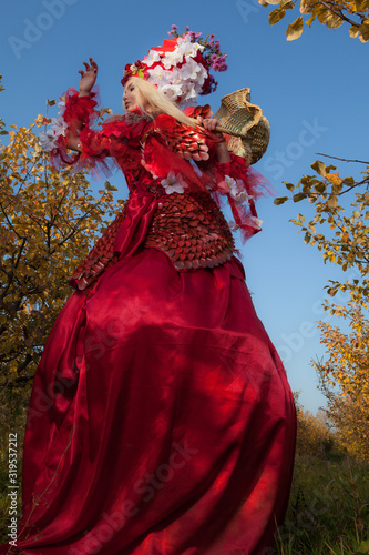 Sensual blond girl in fantasy red fairy tale stylization in apple park.
