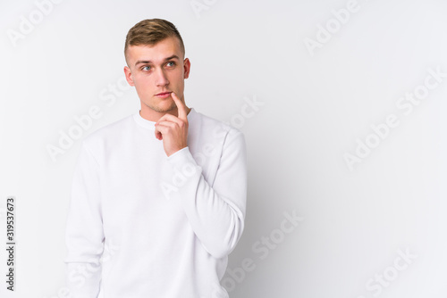 Young caucasian man on white background looking sideways with doubtful and skeptical expression.