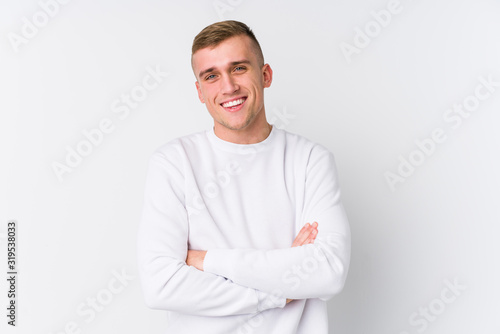 Young caucasian man on white background who feels confident, crossing arms with determination. © Asier