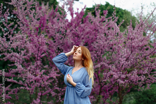 Beautiful dreaming redhead woman in spring time blossom cherrytrees garden. photo