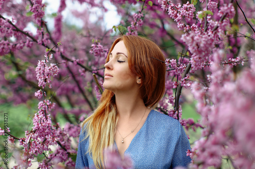 Beautiful dreaming redhead woman in spring time blossom cherrytrees garden.