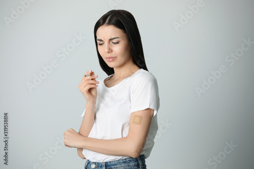 Emotional young woman with nicotine patch and cigarette on light grey background