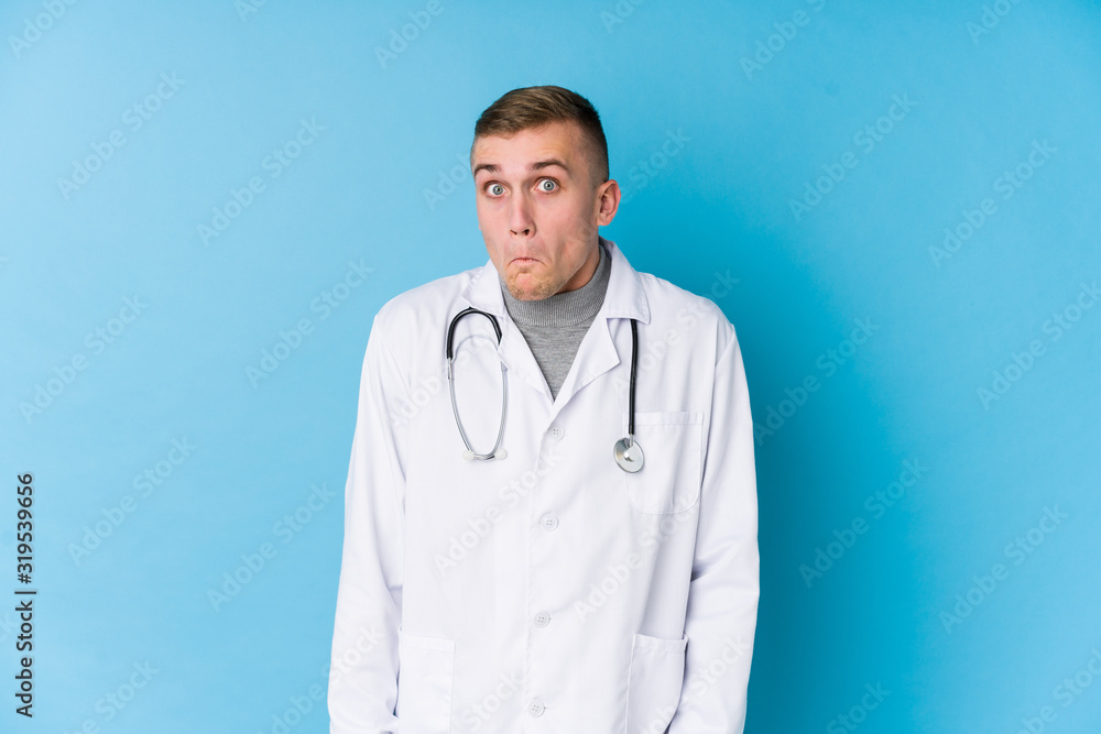 Young caucasian doctor man shrugs shoulders and open eyes confused. Young caucasian doctor man shrugs shoulders and open eyes confused.