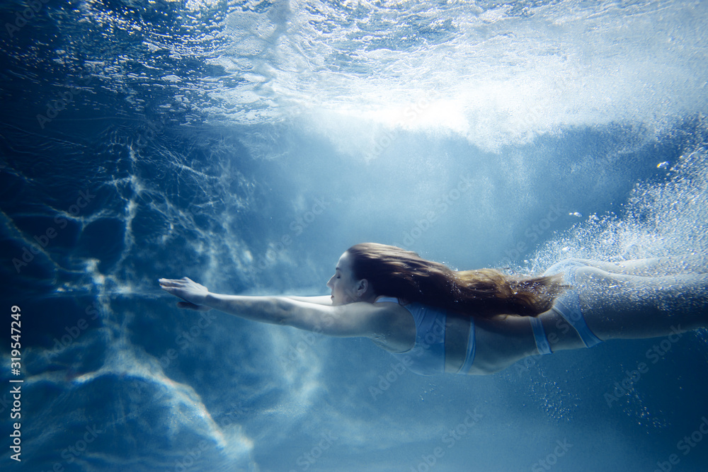 Woman dives under water among the rays of light and air bubbles