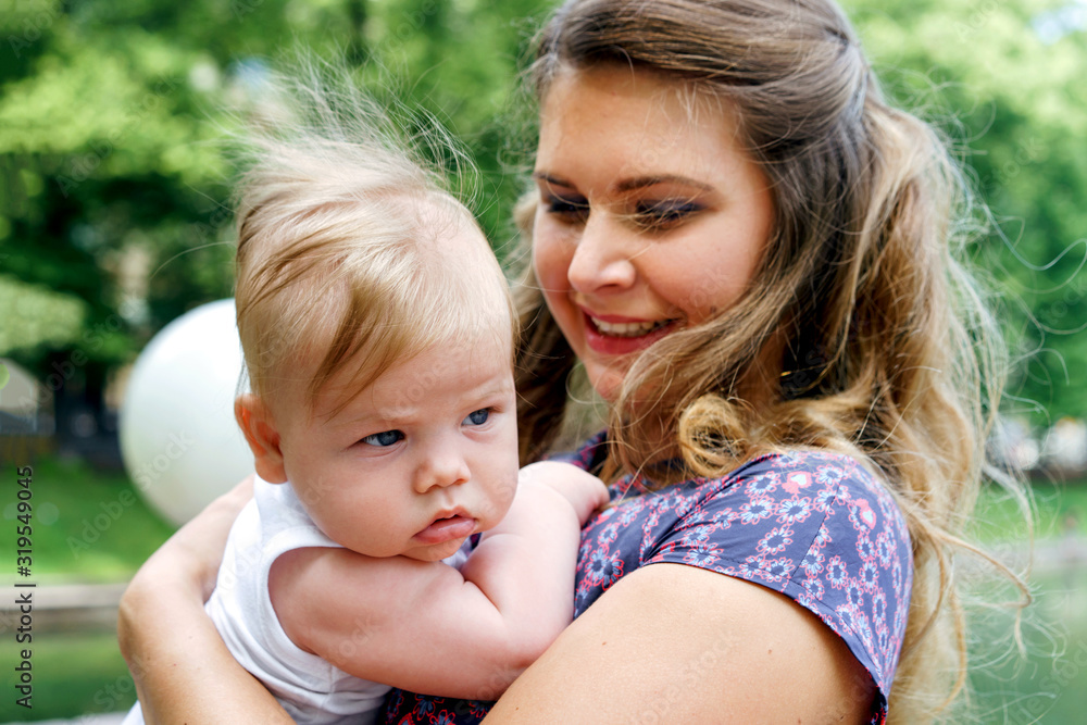 Pretty blond long heared mom and newborn son in her arms in the summer park. The concept summer walking with small children outdoors Pretty blond long heared mom and newborn son in her arms in the summer park. The concept summer walking with small children outdoors