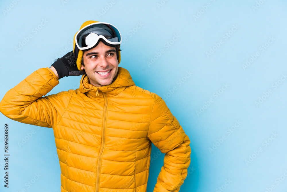 Young skier man wearing snowboard goggles isolated touching back of head, thinking and making a choice. Young skier man wearing snowboard goggles isolated touching back of head, thinking and making a choice.